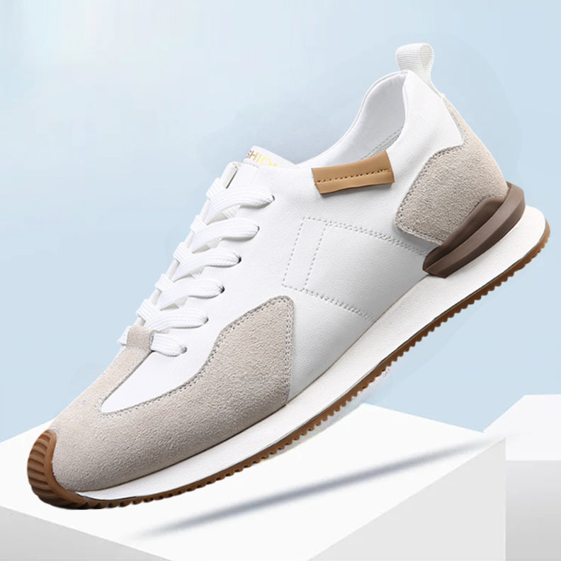 A white athletic sneaker featuring top-grain leather with light gray suede accents, brown heel and toe details, white laces, and a white sole with a brown tread, displayed against a light blue background.
