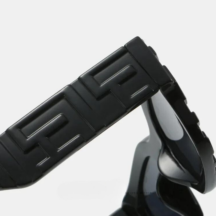 Close-up of a black wristwatch band with a geometric, interlocking G pattern, likely made of ceramic or metal, against a plain light background. The sleek style pairs well with vintage sunglasses featuring anti-glare and UV400 protection.