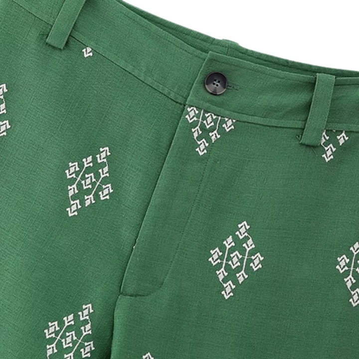 Boho chic pants featuring a white geometric embroidered pattern, black button waistband, belt loops, and a side pocket. These linen trousers have a slightly textured look for added style.