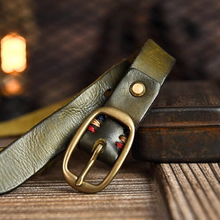 A close-up of a green leather belt with a brass buckle rests on a wooden surface, blending classic country fashion with refined style. Warm lighting in the blurred background evokes elegance fit for Southern ladies.