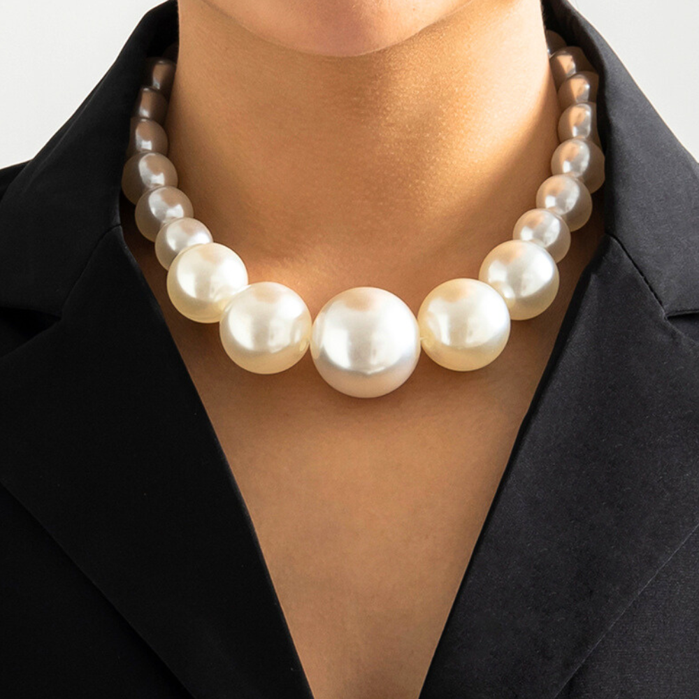 A person wearing a black blazer and a strand of large, round, white pearls around their neck. The statement jewelry features pearls that gradually increase in size toward the center of the necklace.