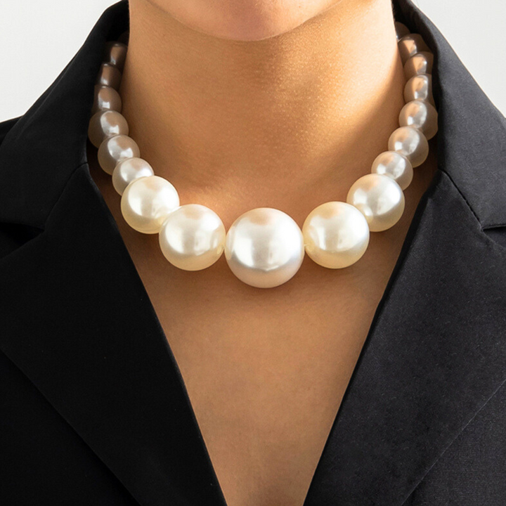 A person wearing a black blazer and a strand of large, round, white pearls around their neck. The statement jewelry features pearls that gradually increase in size toward the center of the necklace.