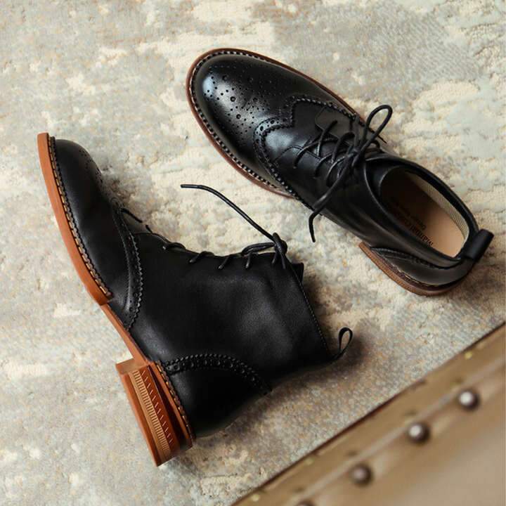 A pair of black genuine leather brogue boots with brown soles is placed on a light textured rug. Featuring decorative stitching and brogue detailing on the toe, theyre perfect for the urban trendsetter.