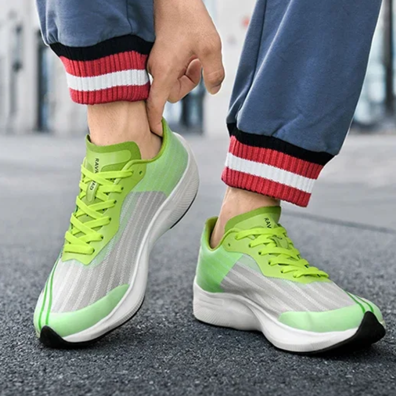 Person wearing blue pants with red and white striped cuffs, adjusting bright green and white athletic sneakers with shock-absorbing sole, standing on a paved surface.