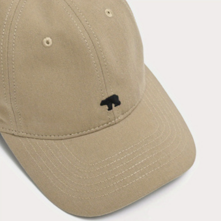 A beige wide brim cap made from premium cotton, featuring visible stitched seams and a small black bear silhouette embroidered on the front for added sun protection.