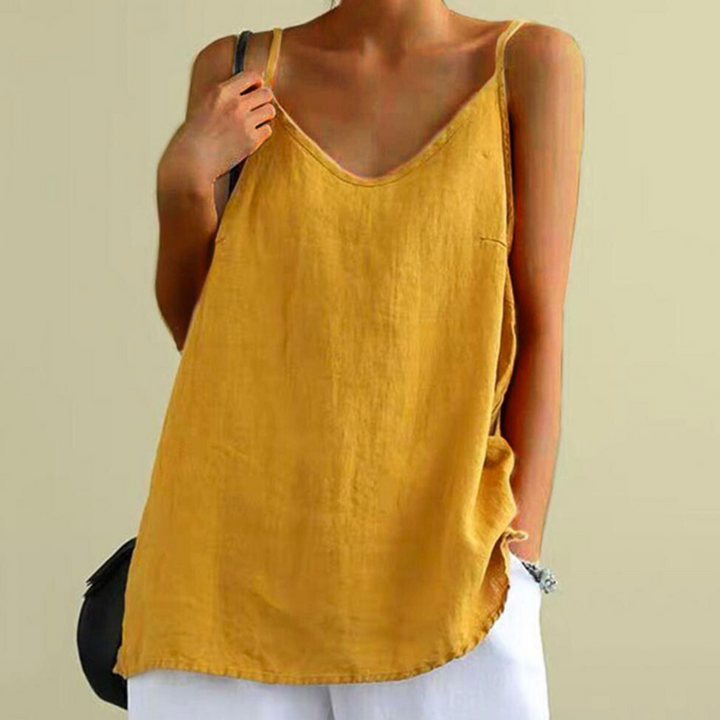 A person wearing an urban-chic mustard yellow camisole with thin straps and a deep V-neck, paired with white pants, stands against a plain light background.