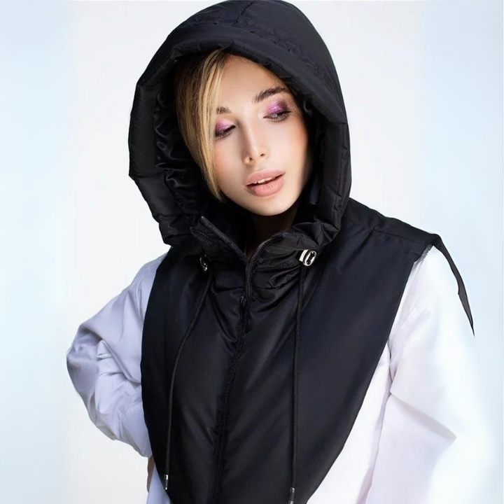 A woman wearing a large, lightweight hooded vest over a white shirt looks slightly downward with her eyes half closed. She has light makeup with purple eyeshadow and blonde hair peeking from under the hooded design.