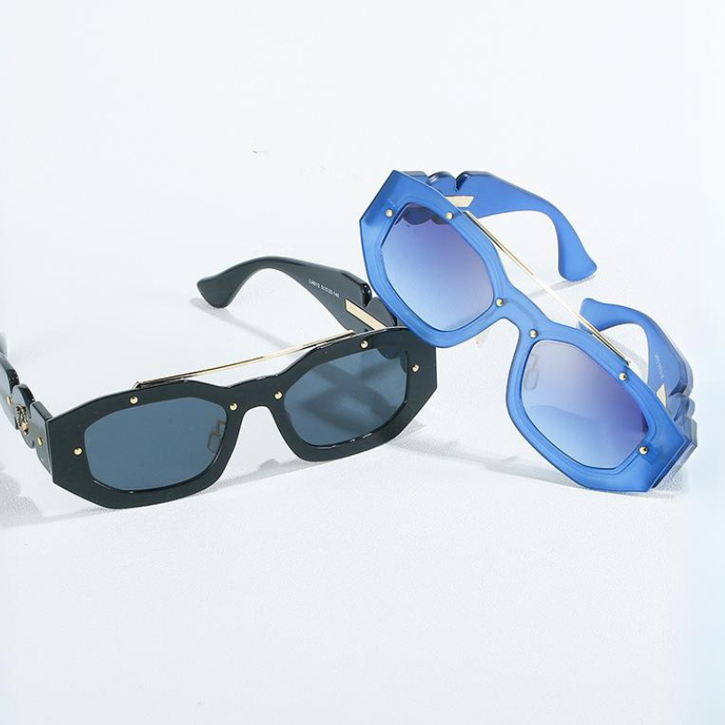 Two pairs of sunglasses on a white surface, both featuring scratch-resistant lenses and gold accents: one with black rectangular frames and dark lenses, the other with blue geometric frames and blue-tinted lenses.