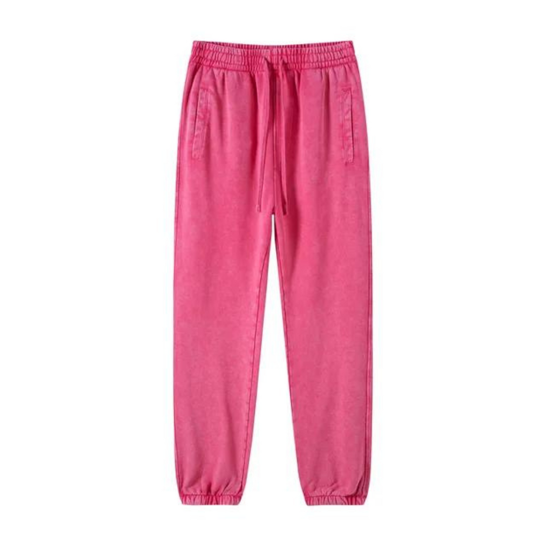 Bright pink sweatpants with an elastic waistband, adjustable drawstring, deep pockets, and tapered cuffs at the ankles, laid flat on a white background.
