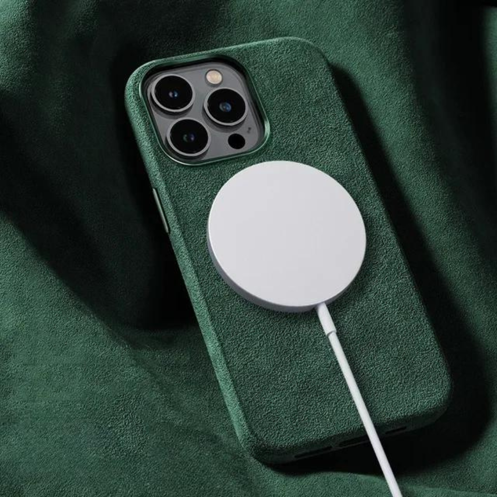 A smartphone with a green case featuring a suede finish is lying on a green fabric surface, with a circular wireless charger attached to its back and a charging cable connected.