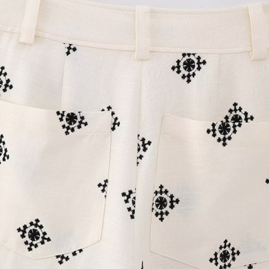Close-up of the back of cream-colored wide-leg trousers with two pockets, decorated with a black geometric embroidered pattern throughout the fabric.