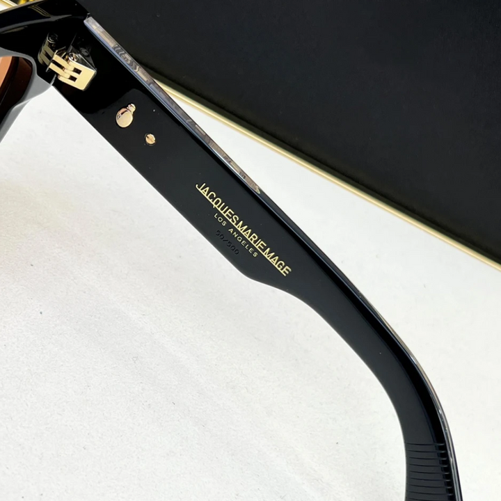 Close-up of the inside arm of black vintage sunglasses with gold hardware. The text Jacques Marie Mage Los Angeles and model information are printed in gold on the inner arm.