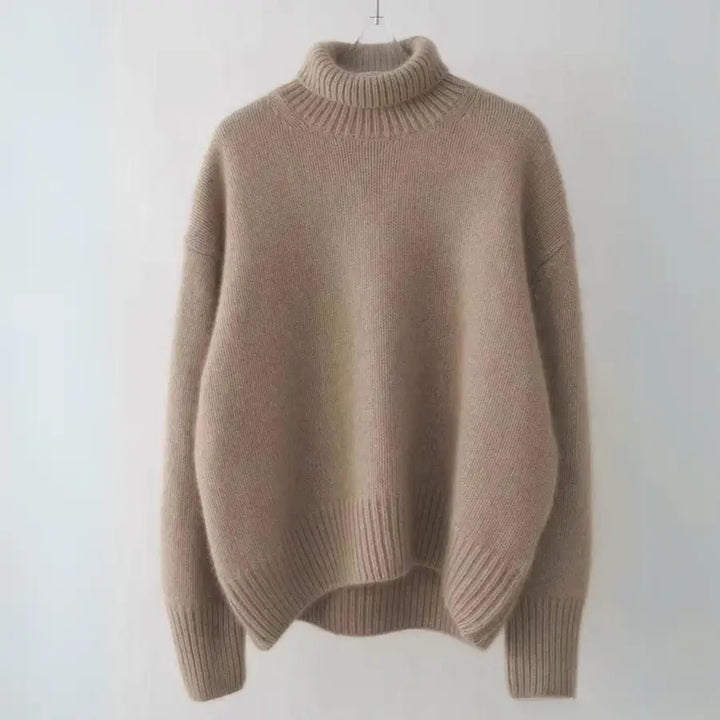 A light brown, cashmere turtleneck sweater with an oversized fit, featuring long sleeves and ribbed cuffs, hem, and collar, hanging against a plain light background.