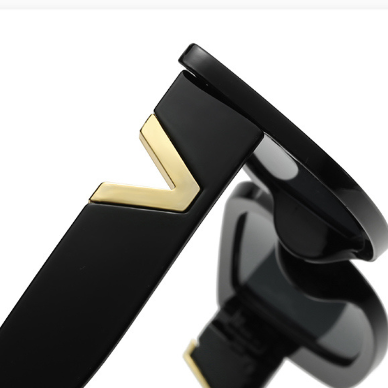Close-up of the black temple arm of designer sunglasses, featuring a gold V-shaped accent. The lens and part of the geometric frame are partially visible in the background.