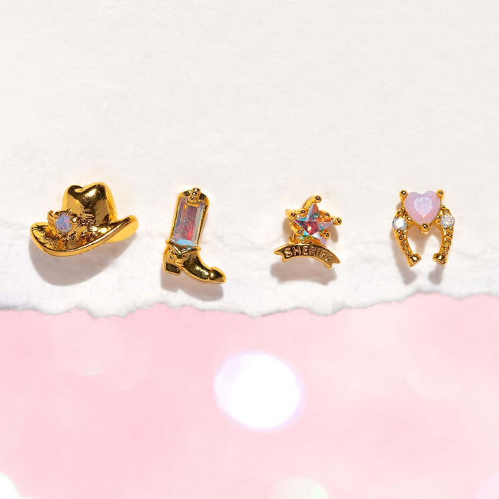Four gold statement earrings displayed in a row: a cowboy hat with a gem, a cowboy boot with a pink stone, a sheriff badge labeled SHERIFF, and urban chic heart-shaped earrings with pink gems, all set on a pink and white background.