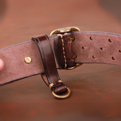 Close-up of a handcrafted belt made from premium leather with a brass buckle and D-ring, featuring detailed stitching, multiple adjustment holes, and a suede-like underside against a brown background.
