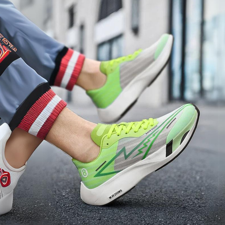 A person wearing light green and gray athletic shoes with a bold zigzag design, neon yellow laces, and a shock-absorbing sole walks on a city street. Their rolled-up pants feature red and white striped cuffs.