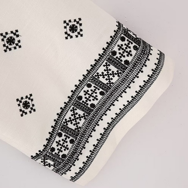 White fabric with intricate black embroidery features geometric and floral patterns along the edge and small square motifs—ideal for crafting boho chic pants or stylish wide-leg trousers.