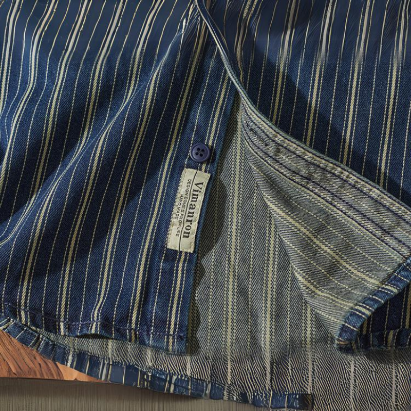 A close-up of a relaxed-fit button-down blue shirt with white vertical stripes, showing its inside seam, hem, blue button, and Vinvoton brand label. The fabric texture and stitching details are clearly visible.