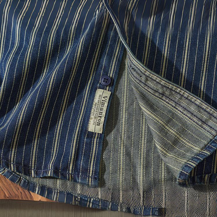 A close-up of a relaxed-fit button-down blue shirt with white vertical stripes, showing its inside seam, hem, blue button, and Vinvoton brand label. The fabric texture and stitching details are clearly visible.