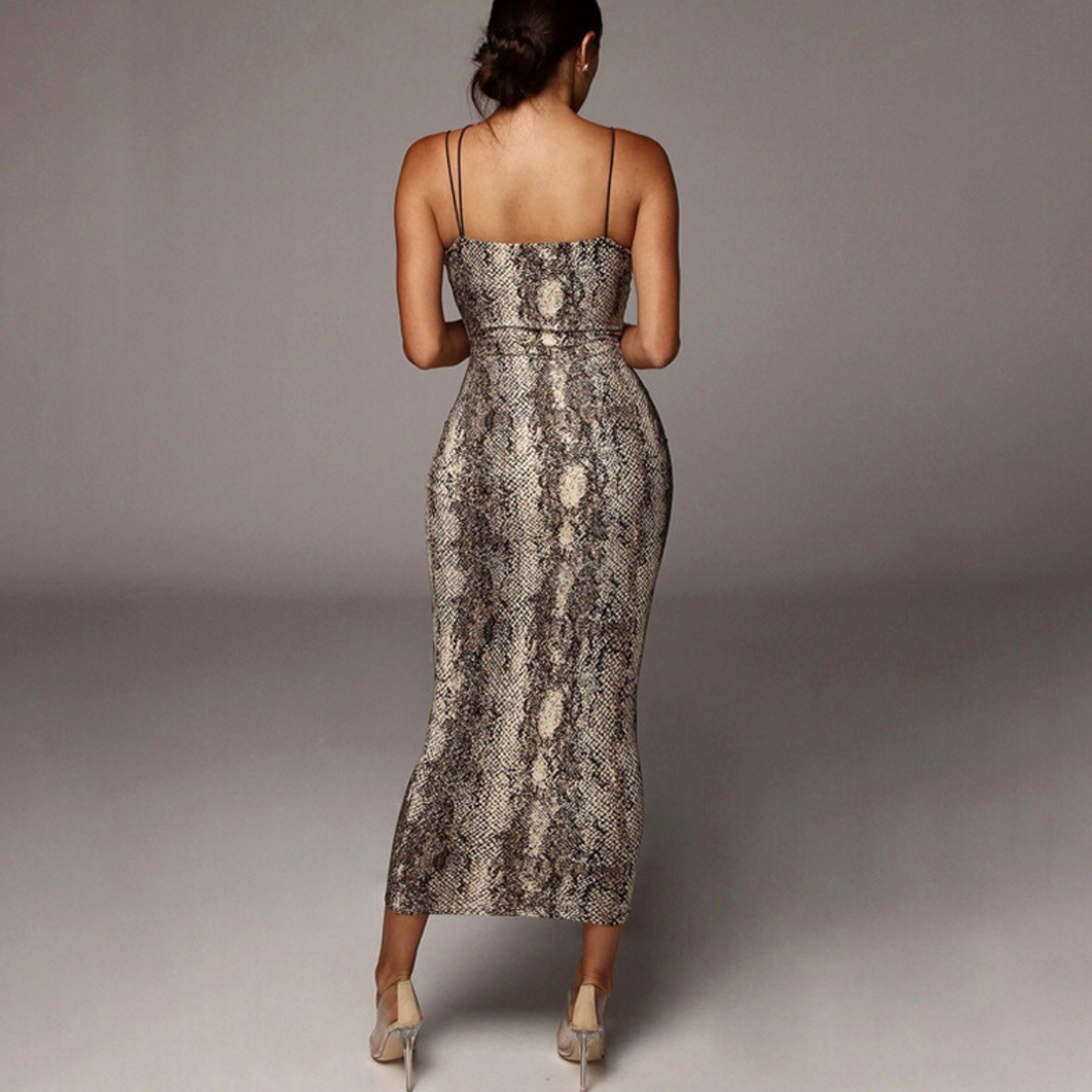 A woman stands facing away, wearing a form-fitting, ankle-length animal print dress with thin straps and beige high heels against a plain, neutral background.