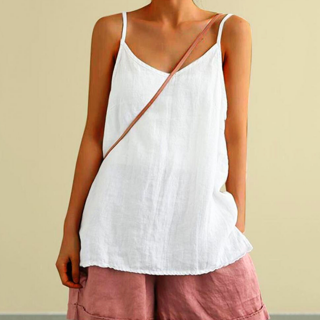 A person wearing a loose urban-chic camisole and pink shorts stands against a plain beige wall, with a thin brown strap diagonally across their chest. Their head is not visible in the image.