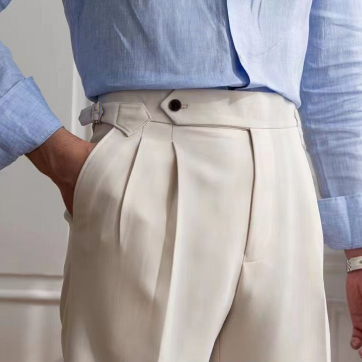 A person wearing a light blue dress shirt tucked into tailored, high-waisted, pleated cream trousers with side adjusters exudes an old money aesthetic. One hand is in their pocket. Only the torso and upper legs are visible.