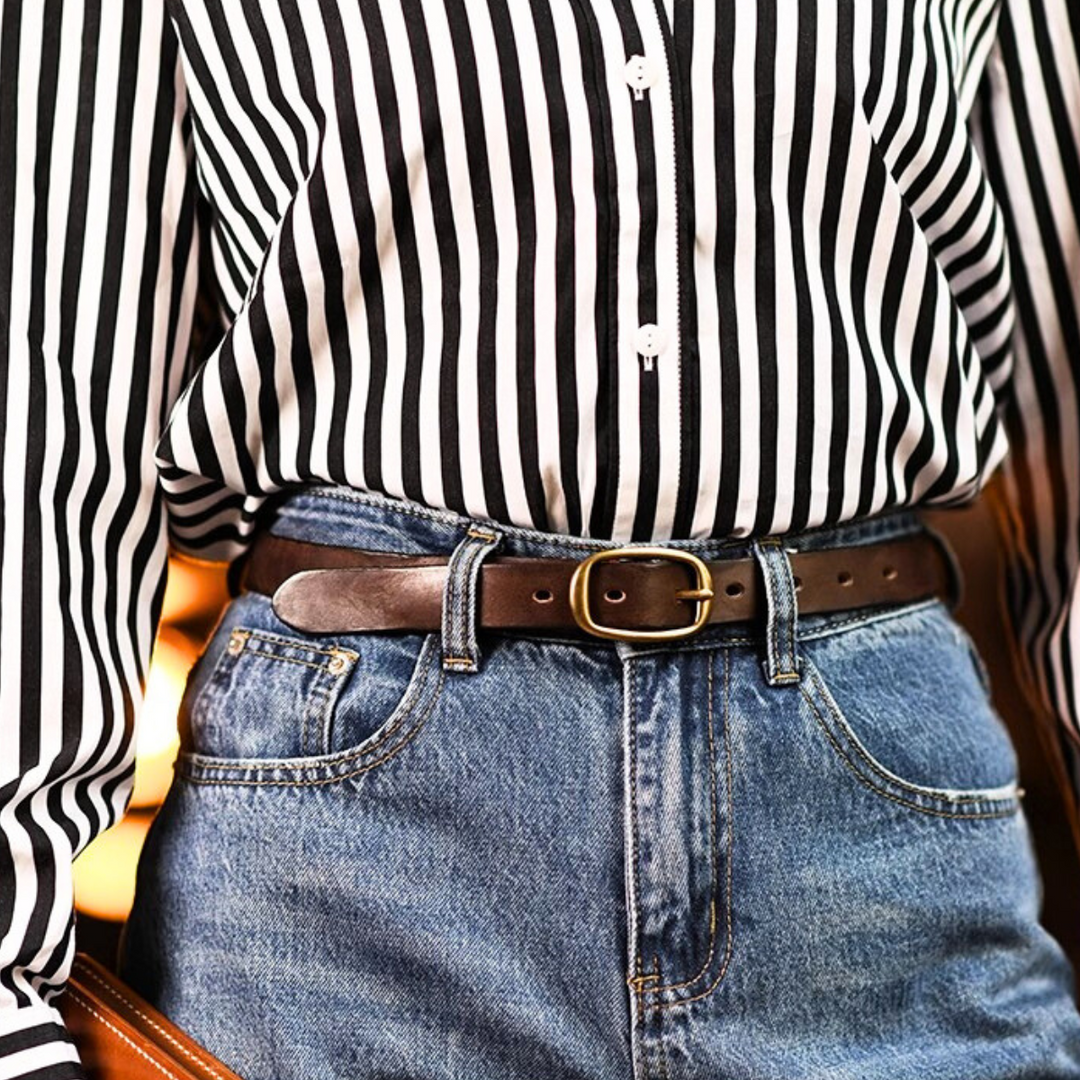 A person wearing a black-and-white vertically striped button-up shirt tucked into high-waisted blue jeans, styled with a classic leather belt featuring a gold buckle—a timeless nod to country fashion.