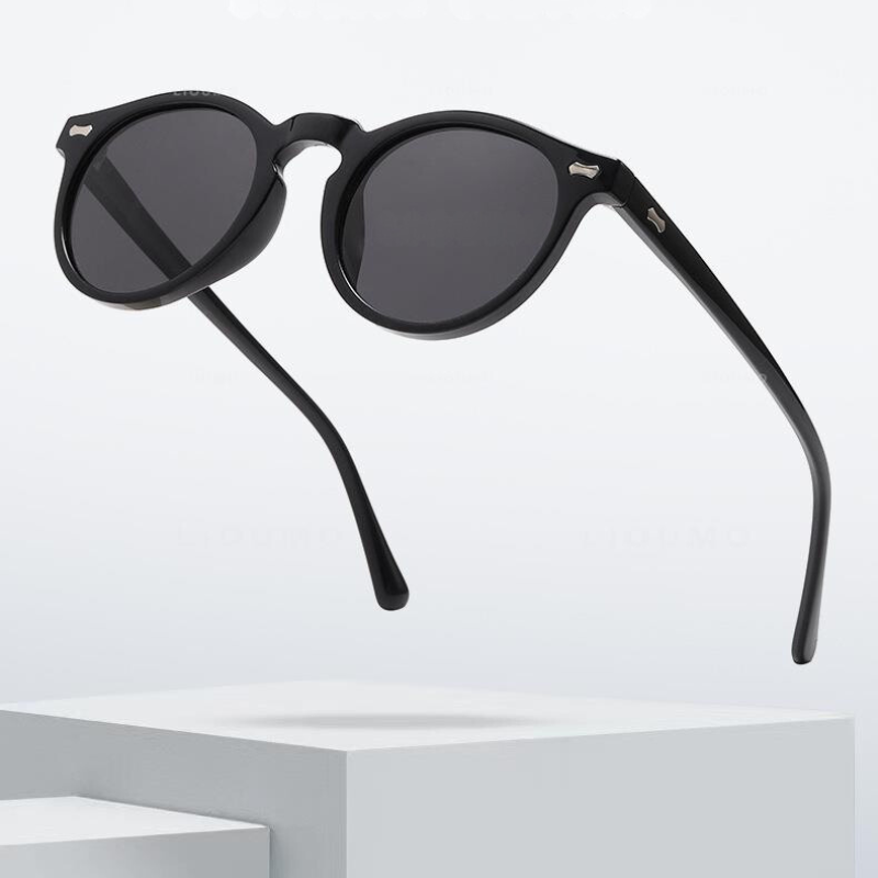 A pair of trendsetting, black round frame sunglasses with dark lenses is shown floating above a white, minimalist platform against a light background.