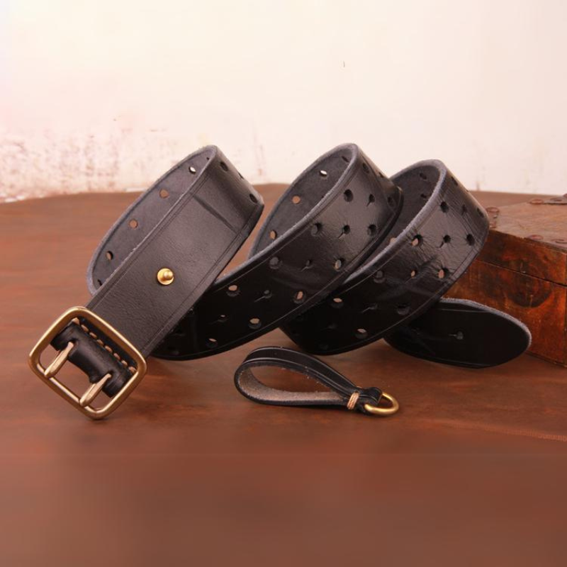 A handcrafted belt made from premium black leather with multiple holes and a brass buckle is coiled on a brown surface, accompanied by a matching leather keychain.