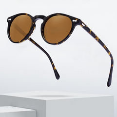 A pair of round frame sunglasses with tortoiseshell rims and brown lenses hovers above a white minimalist platform, blending trendsetting style with everyday versatility against a light background.