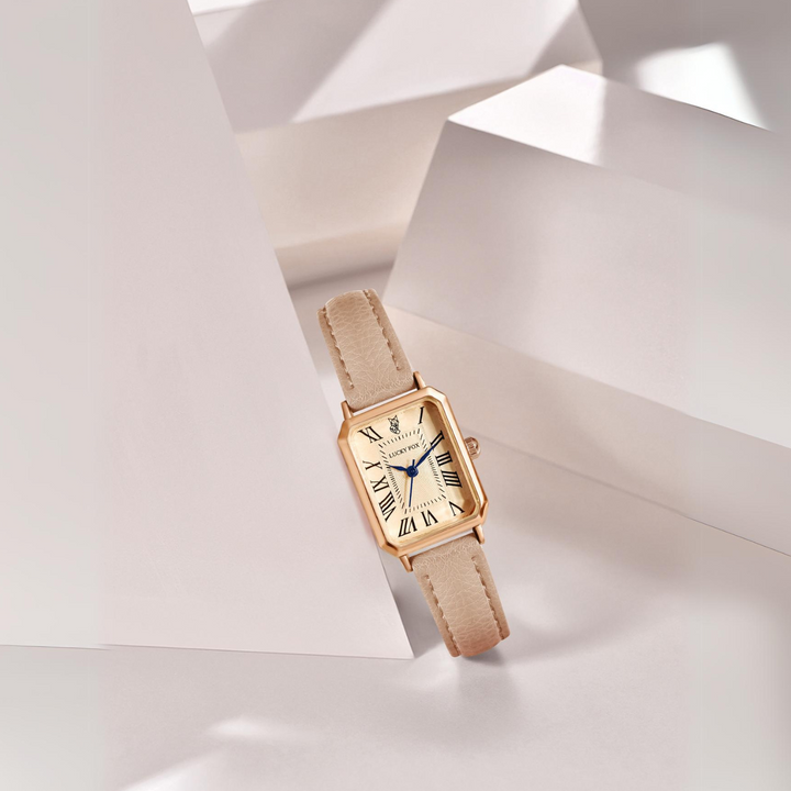 A rectangular face watch with a beige genuine leather strap, Roman numeral markers, and blue hands is displayed among abstract white geometric shapes with soft lighting and shadows.