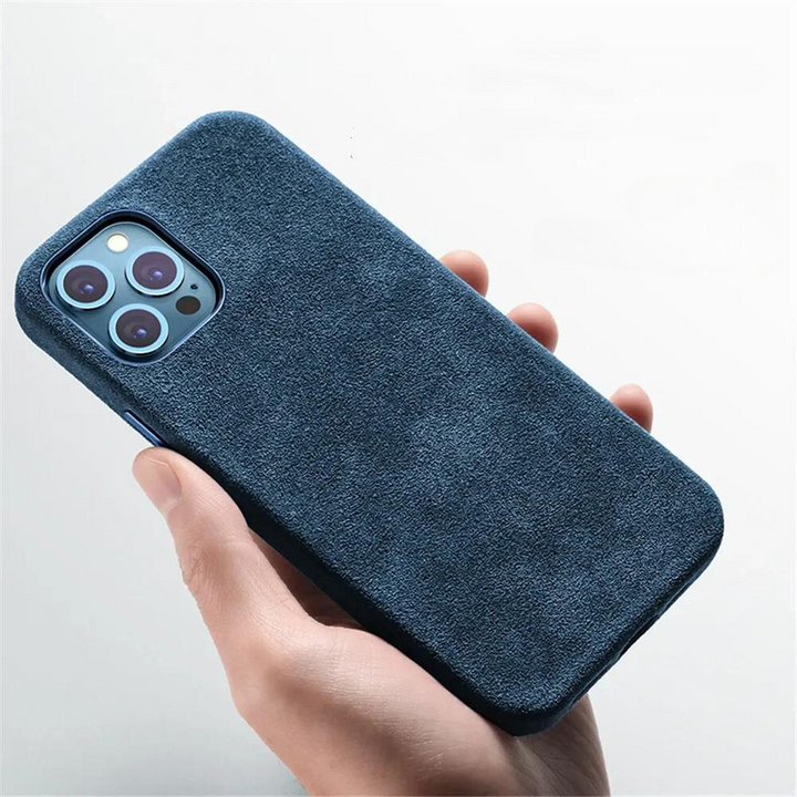 A hand is holding a smartphone with a blue, suede-textured case featuring a protective design. The phone has three rear cameras and a flash, set against a plain white background.