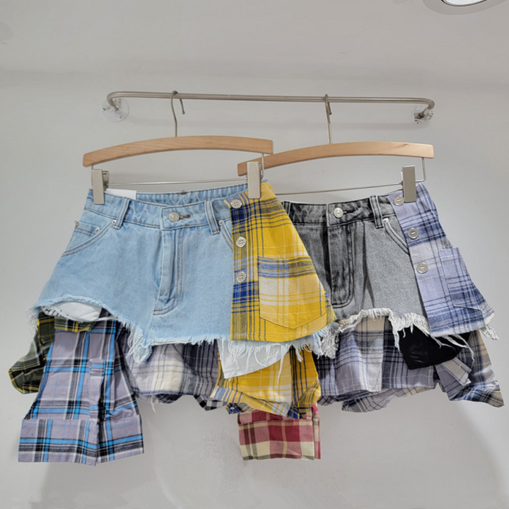 Two unique patchwork skirts hang on wooden hangers. Each skirt features denim and plaid at the top with frayed edges and attached panels, blending eclectic fashion elements in casual and grunge styles against a white background.