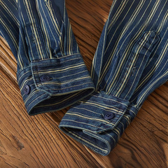 Two blue long-sleeve shirt cuffs with white and yellow vertical stripes rest on a wooden surface. Each cuff, part of a relaxed-fit button-down, is fastened with a dark blue button. The wood has a natural grain and warm tone.