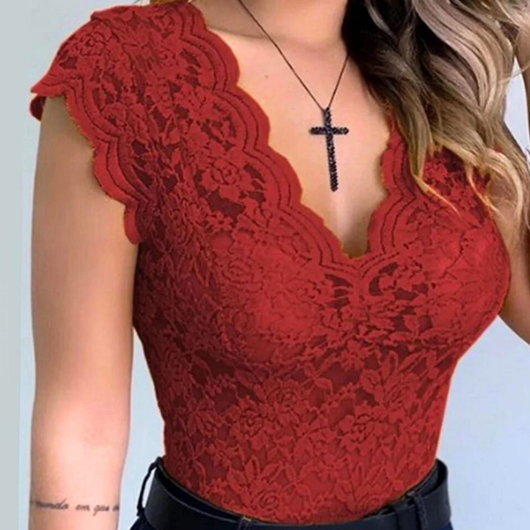 A woman wears a fitted, sleeveless lace top with a scalloped neckline and cap sleeves—perfect for summer fashion—paired with black pants and a black cross necklace. Her hair is styled in loose waves.
