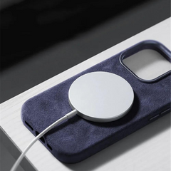 A close-up of a wireless charging pad attached to the back of a smartphone in a dark blue suede finish case, resting on a light-colored surface.