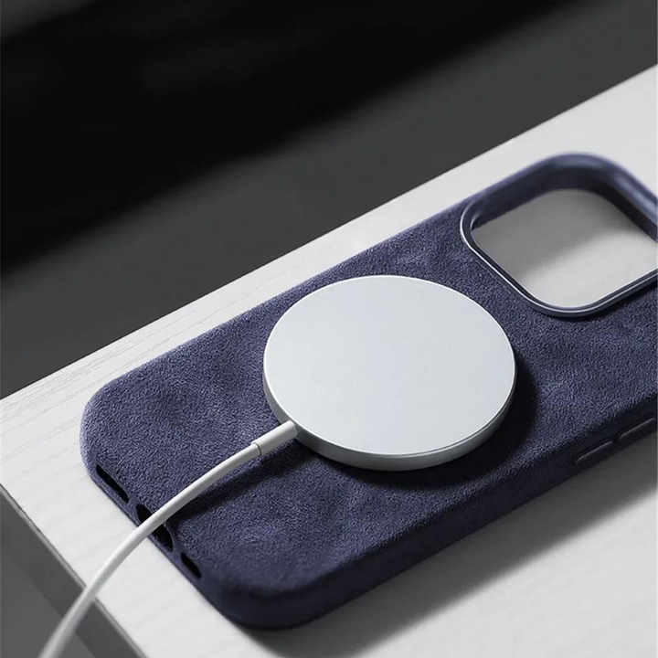 A close-up of a wireless charging pad attached to the back of a smartphone in a dark blue suede finish case, resting on a light-colored surface.