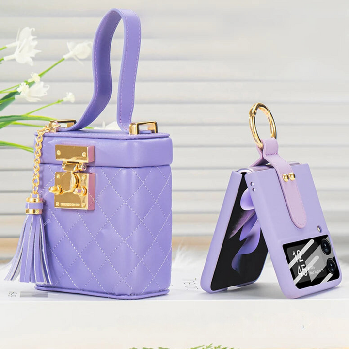 A small, quilted lavender handbag with a gold clasp and tassel sits next to a matching lavender leather phone case with a crossbody strap and gold keyring, both displayed on a white surface.