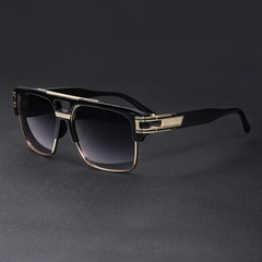 A pair of stylish black and gold geometric sunglasses with rectangular frames and gradient dark lenses, featuring UV400 protection, displayed on a dark surface.