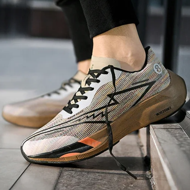 A person wearing colorful, modern athletic sneakers with black laces is standing with one foot on a step. The shoes feature a geometric pattern, bold zigzag design on the side, and a shock-absorbing sole for added comfort.