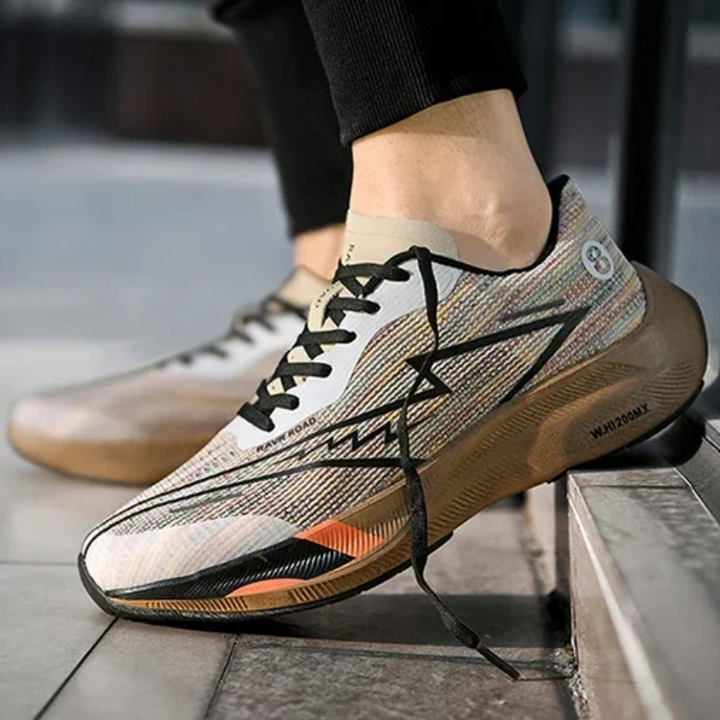 A person wearing colorful, modern athletic sneakers with black laces is standing with one foot on a step. The shoes feature a geometric pattern, bold zigzag design on the side, and a shock-absorbing sole for added comfort.