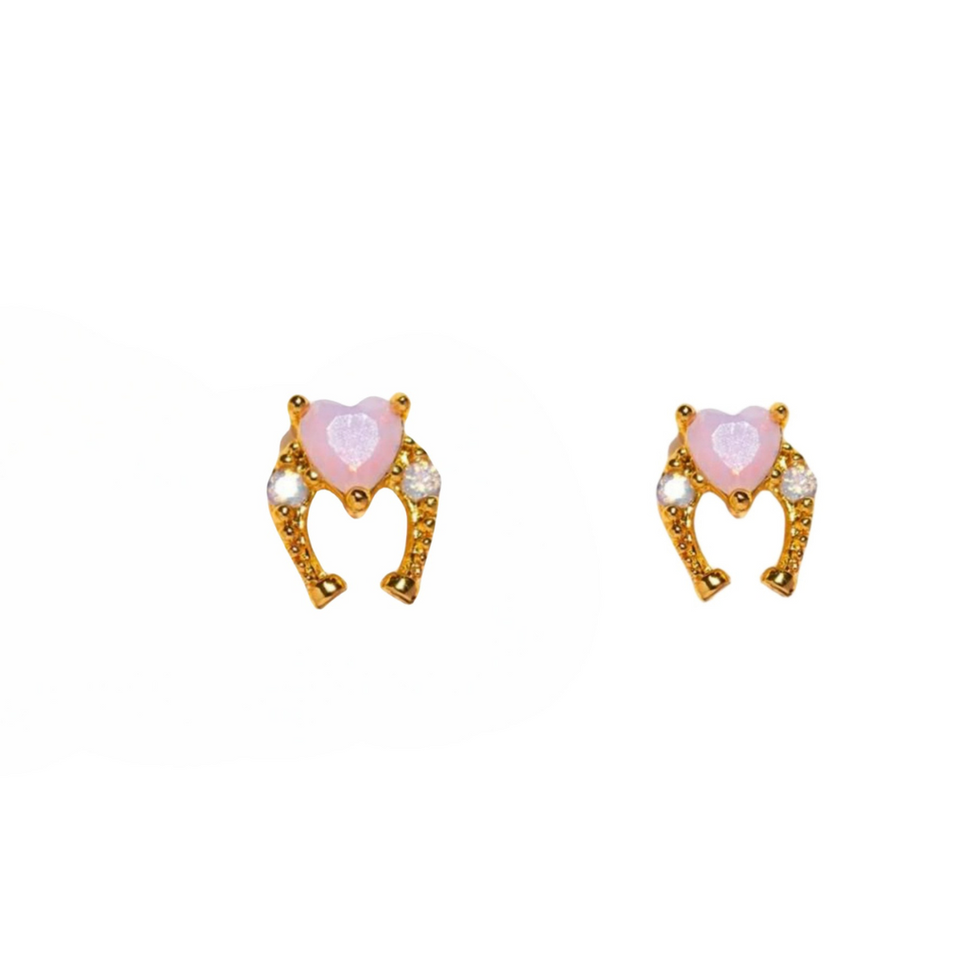 A pair of gold statement earrings with pink heart-shaped stones at the center, adorned with small white and gold accents, displayed on a plain white background.