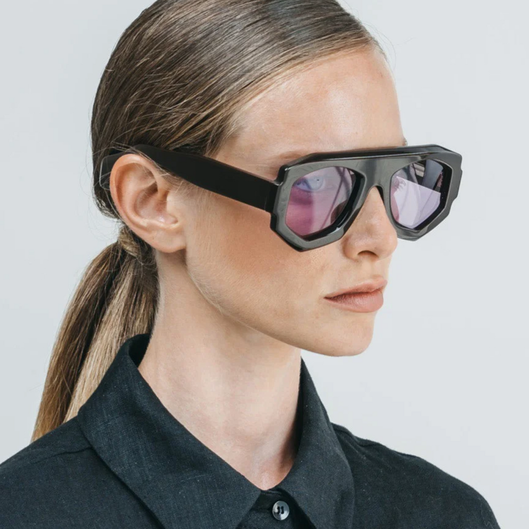 A woman wearing black sunglasses with a geometric frame, crafted from acetate and offering UV400 protection.