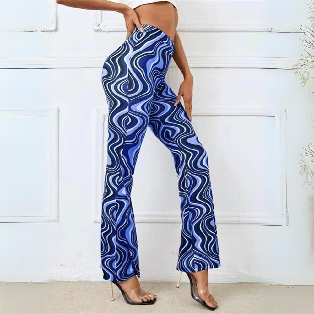 A person wearing retro-inspired, blue and white wavy-patterned psychedelic flare pants stands in profile with one hand on their hip, showing off the trendy statement pants and clear high-heeled shoes in a minimal indoor setting.