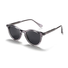 A pair of fashionable eyewear: round frame sunglasses with dark lenses and translucent gray frames, displayed at an angle on a white background.