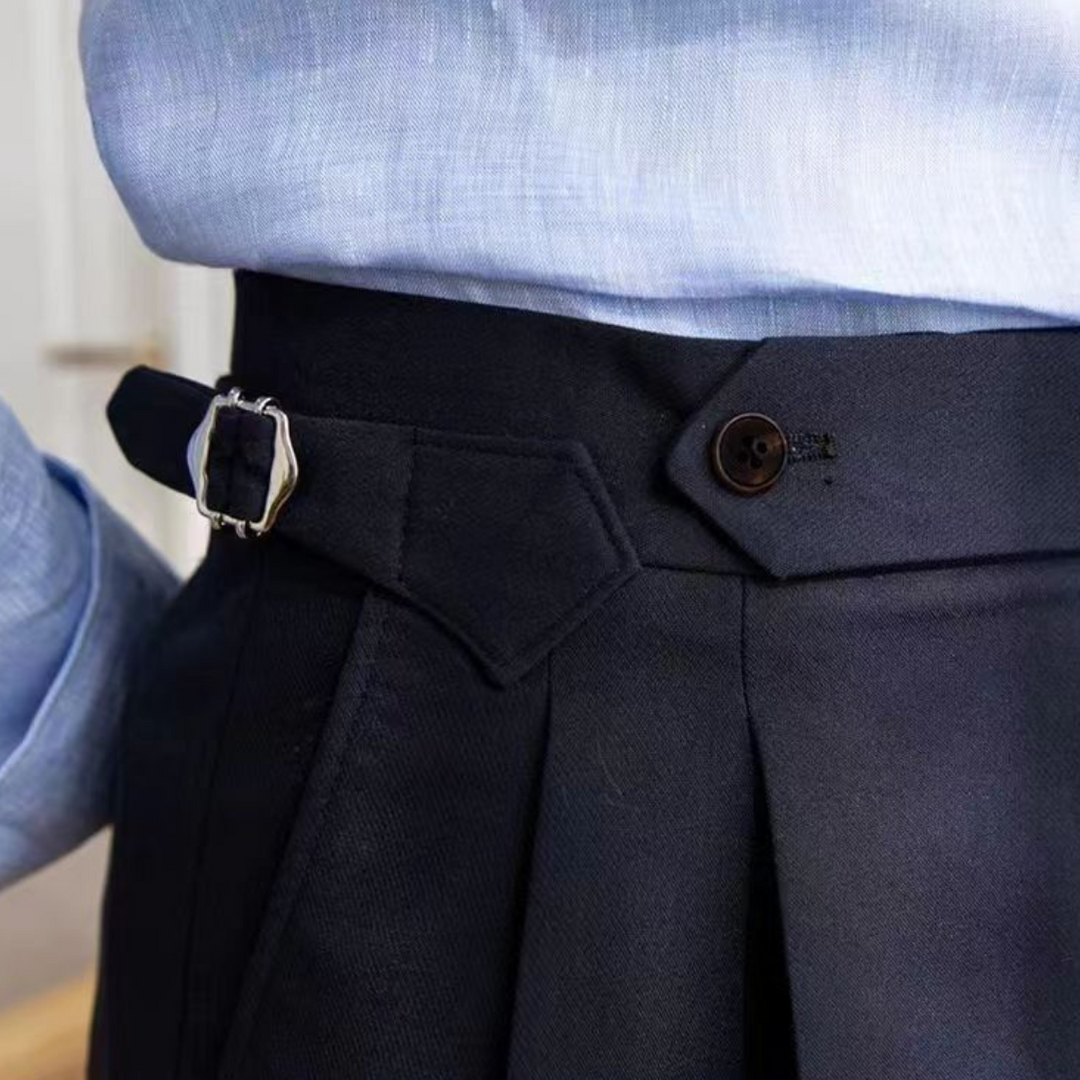 A person wearing a light blue shirt tucked into high-waisted dark pants with a side buckle, pleats, and a buttoned waistband detail, exuding an old money aesthetic and tailored fit.