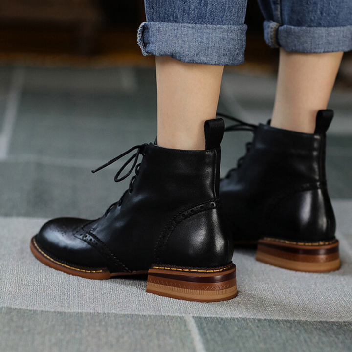 A true urban trendsetter stands on a patterned rug, showcasing genuine leather brogue boots with brown heels and rolled-up blue jeans. The photo, taken from behind, highlights the stylish footwear.