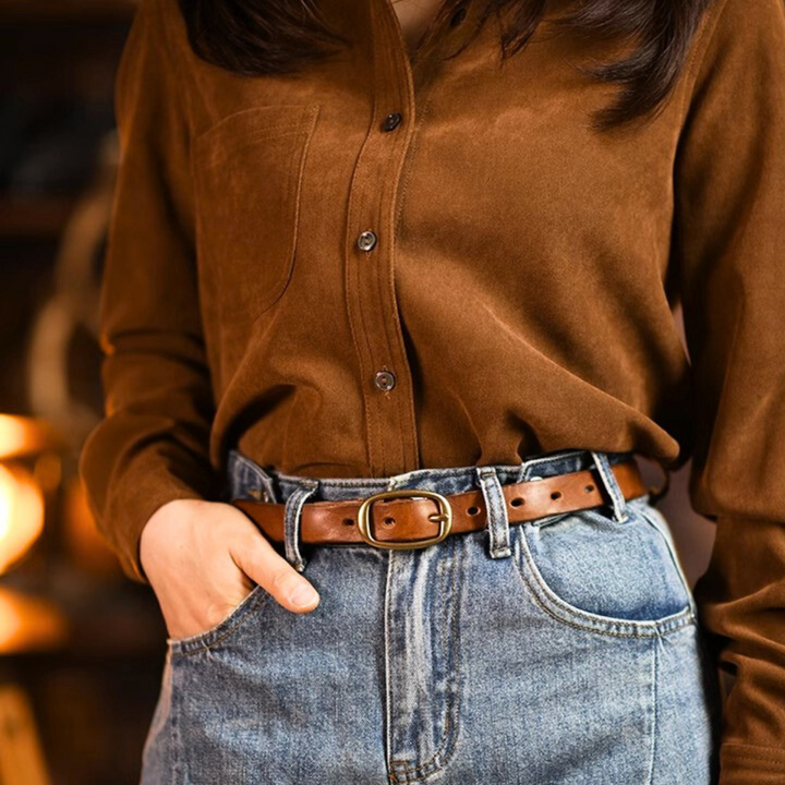 A person channels classic country fashion in a brown button-up shirt tucked into high-waisted blue jeans with a brown leather belt. One hand slides casually into their pocket, while the softly blurred background adds to the timeless style.