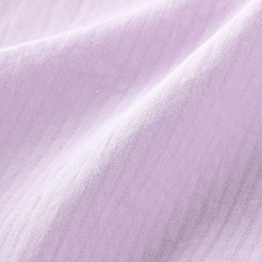 Close-up of soft, light purple fabric with visible weave texture and gentle folds, capturing the smooth, flowing lines of a versatile blouse across the surface.